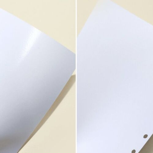 Two white, rounded-corner pages with punched holes, one glossy and one matte, lie atop a light beige surface, highlighting their dual surfaces.