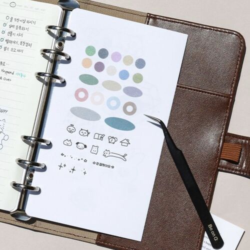 The open sticker book reveals colorful oval and circular stickers on double-sided pages, with a brown leather cover and metal rings for organization.