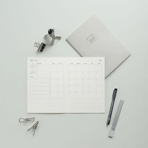 A minimalist, flat-lay view showcases the open July 2027 monthly spread with clean lines, subtle red accents, and neatly organized sections on a soft gray background.