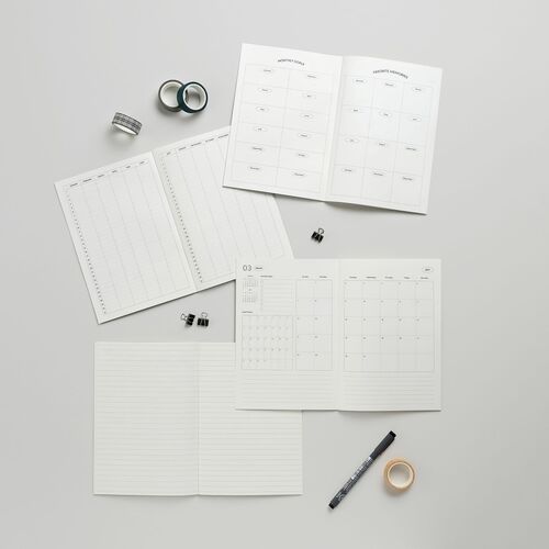 Open planner pages reveal clean, minimal layouts with neatly organized sections for goals, memories, and monthly planning, accented by subtle grid lines.