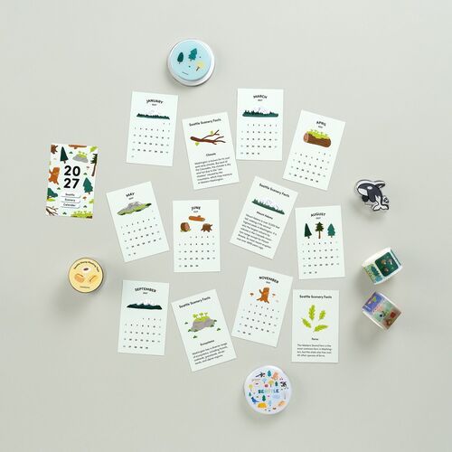 Scenic Seattle-themed calendar sheets with colorful illustrations and educational facts, displayed in a flat lay arrangement on a neutral background.