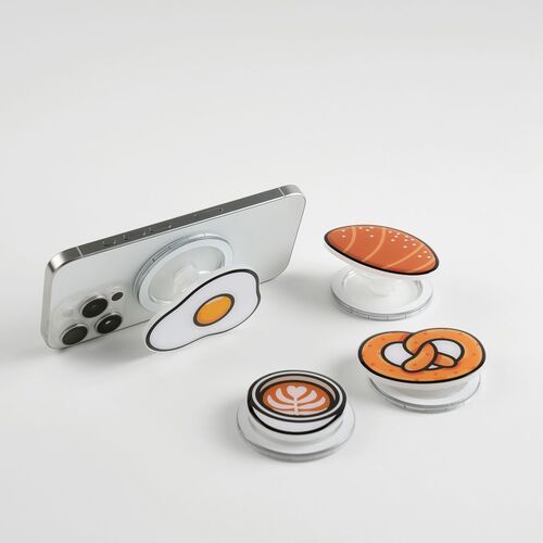 The image showcases four adorable food-inspired magnetic phone grips with colorful, glossy designs, arranged around a silver smartphone on a white background.