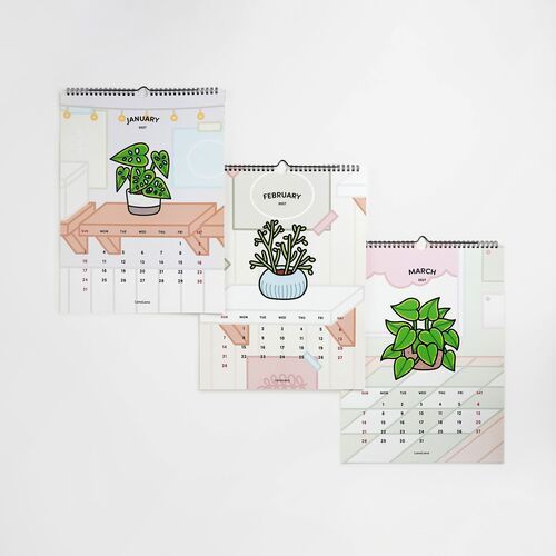 Three vibrant, houseplant-themed calendar pages hang against a white wall, showcasing colorful illustrations and clear monthly layouts.