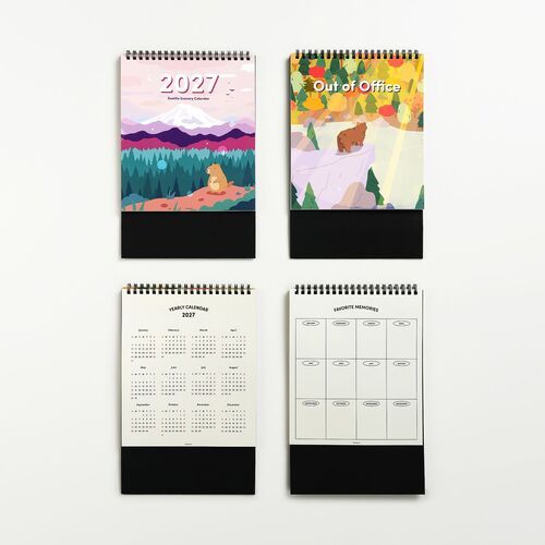 Four spiral-bound calendars featuring vibrant mountain and forest illustrations, with black stands and clean white backgrounds highlighting their colorful covers and pages.