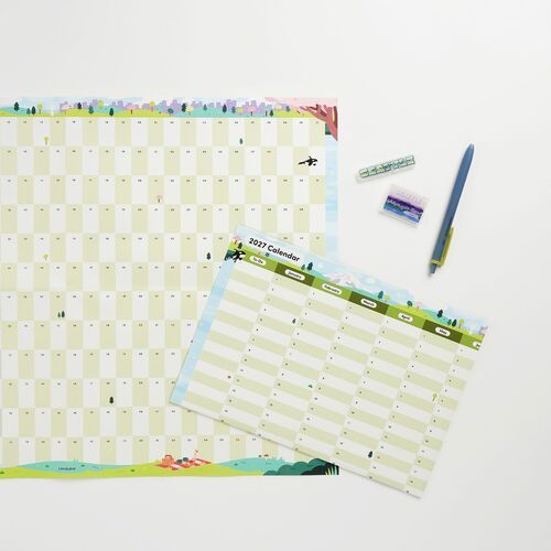 A layered product scene pairs the wall poster with a smaller calendar and stationery, showing how it fits a desk setup.
