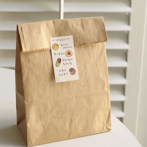A kraft paper bag with a small, colorful handwritten menu sticker, set against a neutral background with white slatted blinds.
