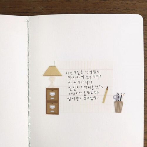 A close-up of a notebook page decorated with cute, tiny stickers of a lamp, a shelf, and stationery, adding cozy charm.