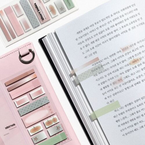 The image showcases a collection of pastel-colored sticky notes with various shapes and designs, arranged neatly beside an open book with highlighted text.