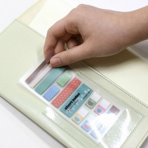 A hand peeling back a clear sticky note sheet revealing colorful, patterned notes in pastel shades on a soft, light-colored surface.