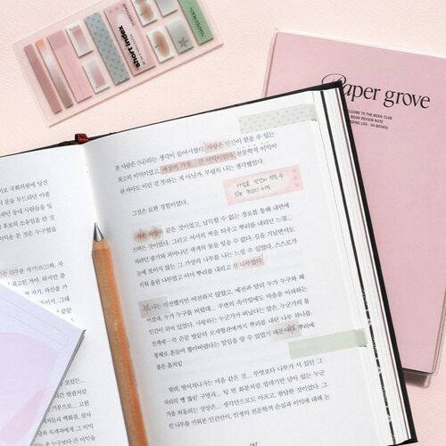 The open book reveals handwritten notes highlighted with pastel-colored sticky notes, set against a soft pink background with additional sticky note designs nearby.
