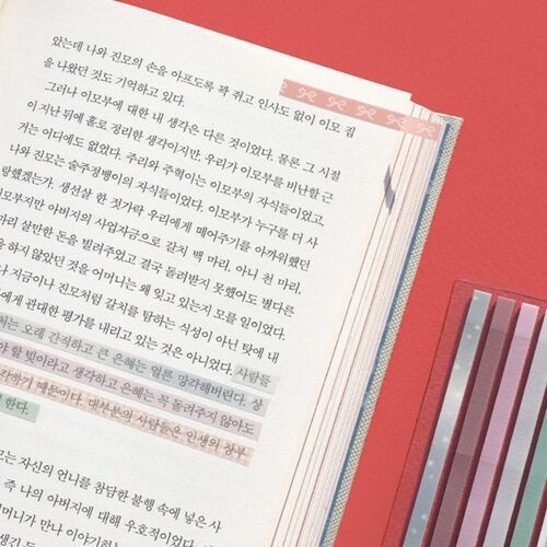 A close-up of a book page with a long, pink sticky note at the top, featuring a delicate bow pattern, complemented by colorful patterned sticky notes on the side.