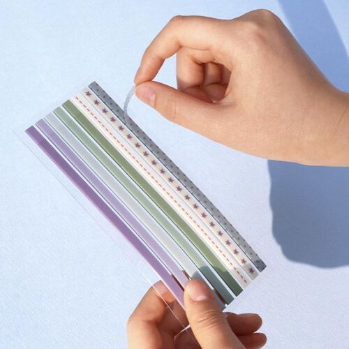 A hand holds a transparent, perforated strip featuring pastel-colored patterns, emphasizing the product's tearable and decorative qualities.