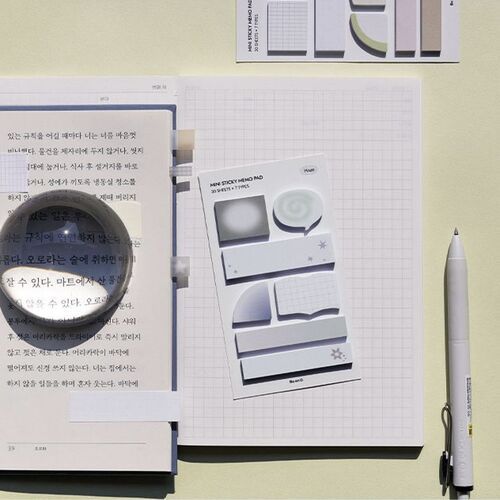 A neatly arranged workspace featuring the Mini Be On D Sticky Note Set with various shapes and shades, complemented by writing tools and paper.