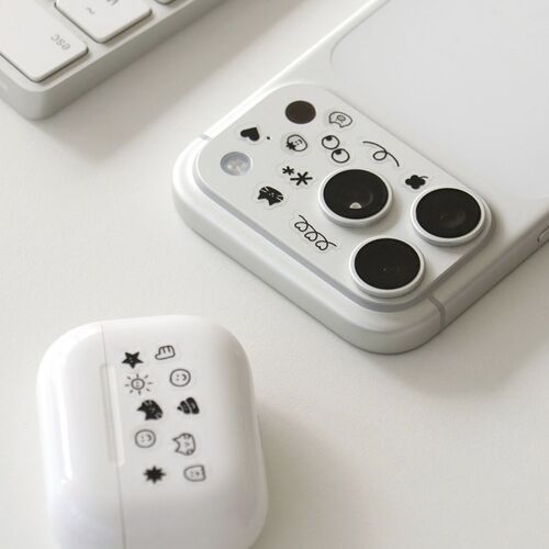 The image features a white smartphone with cute doodle stickers on its camera area, paired with a matching stickered case and a portion of a white keyboard.