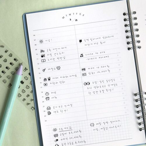 The open planner showcases a neat layout with playful doodle icons, complemented by a pastel pen and additional sticker sheets nearby.