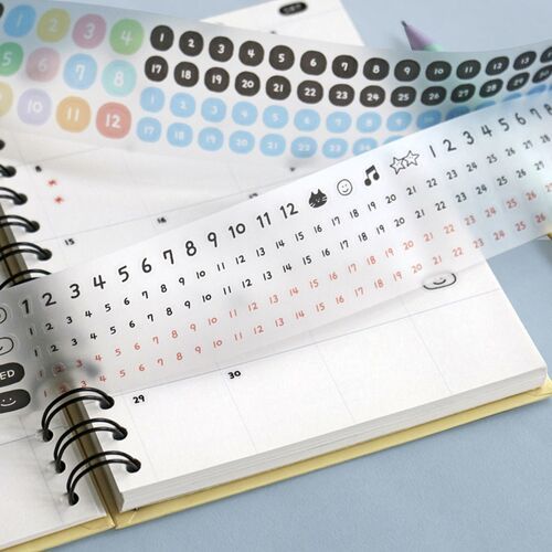 Colorful sticker strips with playful icons and numbers are displayed on a spiral planner, highlighting the product's fun, organized aesthetic.