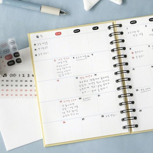 The image showcases a cheerful planner page adorned with colorful stickers, alongside a matching sticker sheet and a cute pen, all set on a soft blue surface.