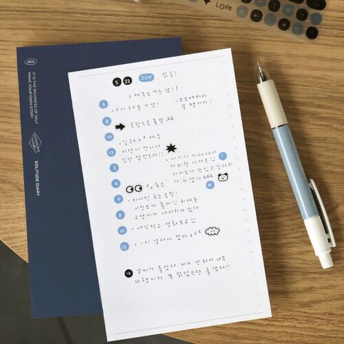 A cheerful scene featuring a white sheet with blue doodle icons and handwritten notes, complemented by sticker sheets and a pen on a wooden surface.