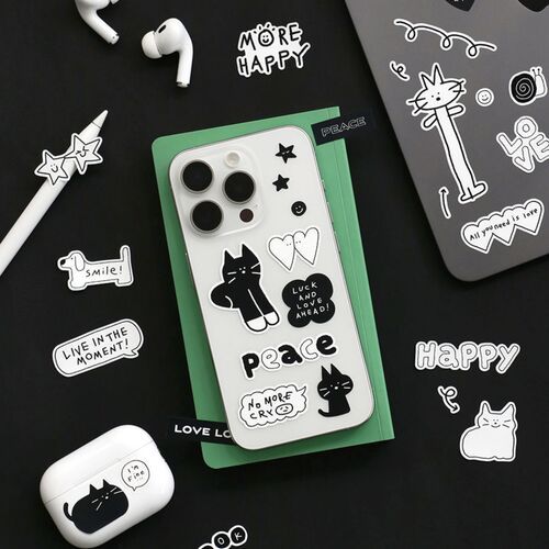 A white phone case decorated with black and white doodle stickers featuring cats, hearts, and stars, set against a dark background with additional sticker accessories.