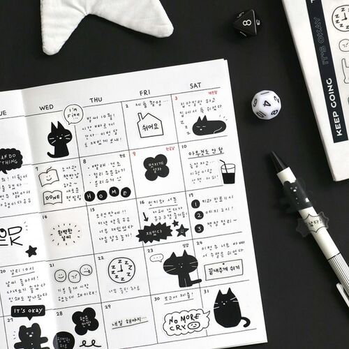 A weekly planner page decorated with playful black doodle stickers of cats, stars, and speech bubbles, set against a black background with gaming dice and a pen nearby.