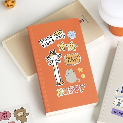 Bright orange doodle journal with playful cat and star stickers, surrounded by other stationery items on a white surface.
