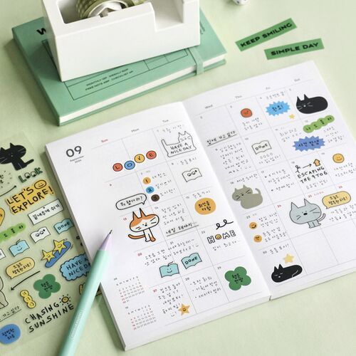 A flat-lay of a planner open to a colorful weekly spread, surrounded by cute stickers, a pastel pen, and decorative tape on a mint green background.