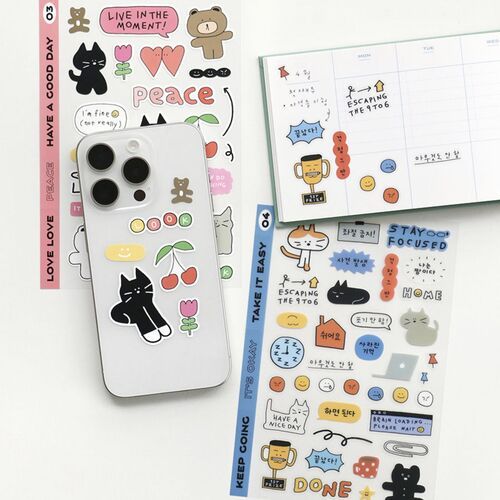 A clear phone case adorned with playful black doodle stickers featuring cherries, a cat, and a smiley face, placed on colorful planner pages.