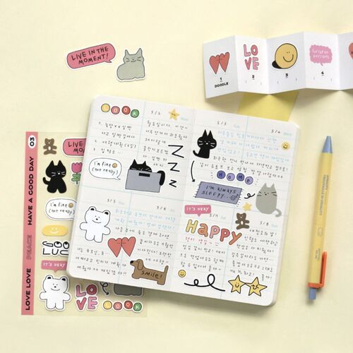 Colorful doodle stickers featuring cats, bears, and icons are displayed on a cheerful, pastel yellow background, with a decorated journal nearby.