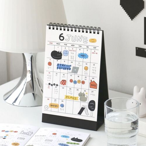 The photo showcases a playful June calendar featuring adorable cat and animal illustrations, complemented by stationery accessories and a glass of water.