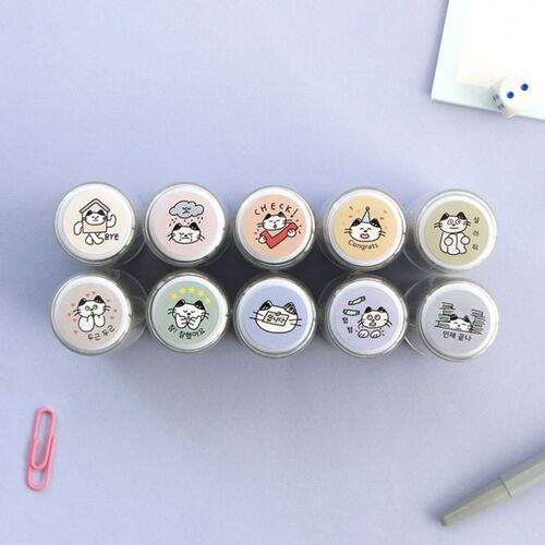 A top-down view of ten small, round self-inking stamps featuring cute cat illustrations with Korean text, arranged neatly on a pastel purple surface.