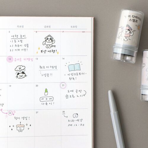 Two cute, illustrated self-inking stamps with playful cat designs sit beside a colorful, decorated weekly planner page filled with charming doodles.