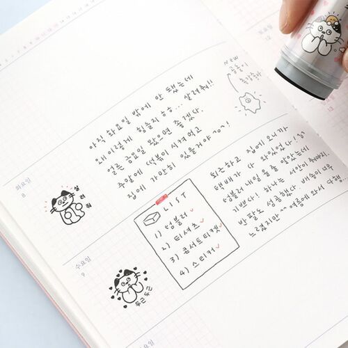 The stamp features a cute, cartoon-style cat illustration with expressive eyes and tiny paws, positioned above handwritten notes in a planner.