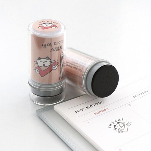 Two cute cat-themed self-inking stamps with pink and gray accents are displayed on a white surface, one standing upright and the other lying down.