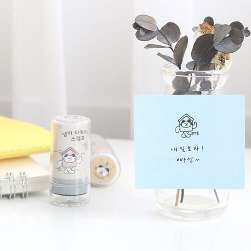 The image showcases a cute, compact self-inking stamp featuring a playful cat illustration, positioned beside stationery and a note with a matching cat character.