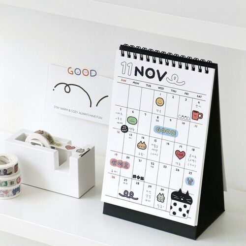 The desk features a playful calendar with cute doodle stickers, complemented by washi tapes and organized stationery in a bright, minimalist setting.