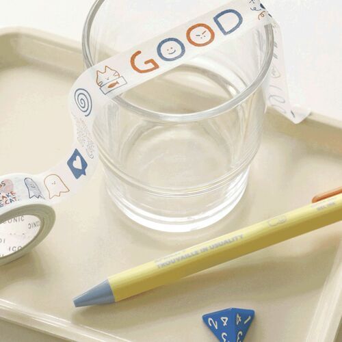 The image showcases a roll of doodle masking tape draped over a clear glass, with playful doodle designs and vibrant colors visible on the tape.