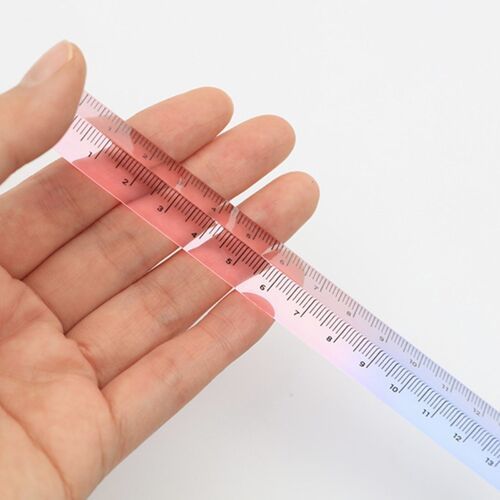A hand holding a transparent, gradient pink triangular ruler against a plain white background, emphasizing its clarity and modern design.