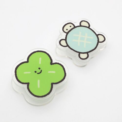Two cute acrylic magnet clips featuring cheerful, smiling characters—a green four-leaf clover and a blue turtle—set against a plain white background.