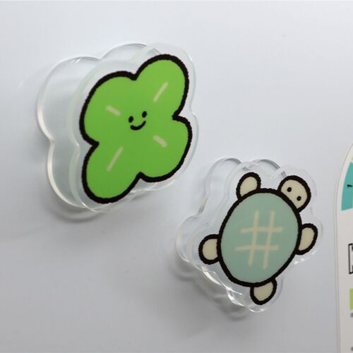 Two cute acrylic magnet clips featuring cheerful green clover and adorable turtle designs are displayed on a white surface, highlighting their playful charm.