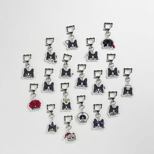 A collection of 18 colorful acrylic tuxedo cat emoji key rings arranged in a scattered pattern on a white background, showcasing varied expressive faces and accessories.