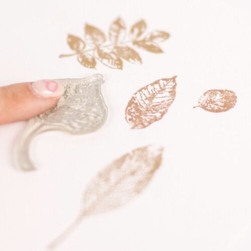 A close-up of a flexible, transparent silicone stamp being pressed onto paper, showcasing detailed leaf and nature-themed impressions.