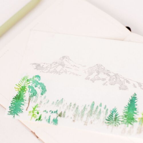 A delicate, watercolor-style illustration of mountain scenery with lush green trees, printed on textured white paper, accented by a soft green pen.