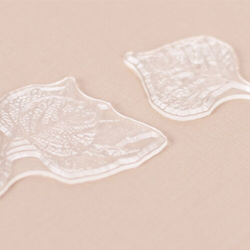Two transparent silicone stamps with intricate leaf and branch patterns rest on a soft pink background, showcasing detailed nature-inspired designs.