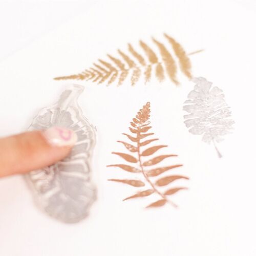 A close-up view of a flexible, translucent silicone stamp being pressed onto a white surface, revealing detailed leaf impressions.