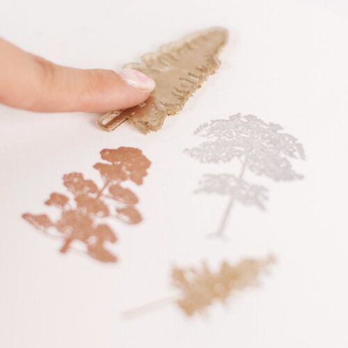A hand presses a soft silicone stamp onto white paper, revealing intricate, detailed leaf and tree designs for crafting projects.