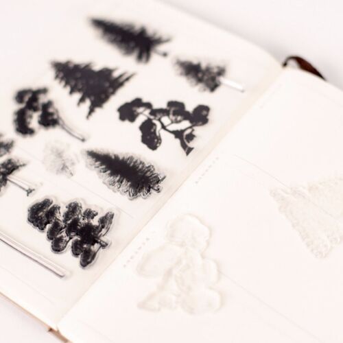 Black silicone stamps featuring detailed trees, leaves, and mountain scenes are arranged on a white surface, highlighting their intricate designs.