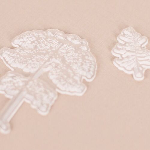 Two transparent silicone stamps with intricate leaf and tree designs rest on a soft beige background, highlighting their detailed craftsmanship.