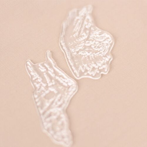 Two transparent silicone stamps with intricate leaf and mountain designs rest on a soft beige surface, highlighting their flexibility and fine detail.