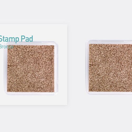 Two metallic shimmer stamp pads, one labeled bronze, with textured surfaces reflecting light, positioned on a clean, light gray background.