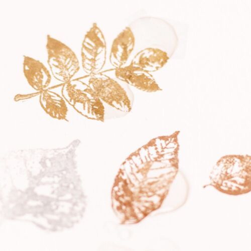 A close-up of a metallic shimmer stamp pad in bronze, with stamped leaves and a leaf outline, showcasing its shiny, reflective finish.